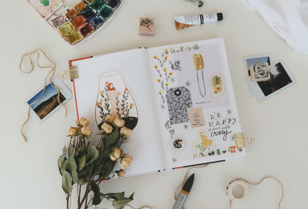 Ein selbst gestaltetes Familienalbum zum Vatertag liegt aufgeschlagen auf einem Tisch; drumherum befinden sich Blumen, Fotos und Bastelutensilien.