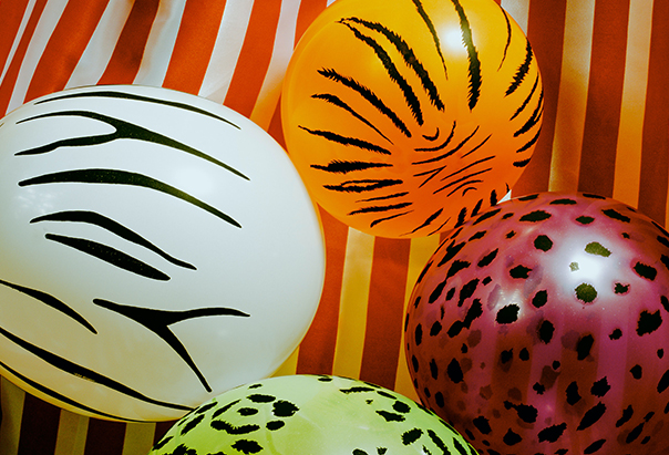 Zu sehen sind bunte Luftballons mit Tier-Print vor einem rot-weiß gestreiften Hintergrunf.