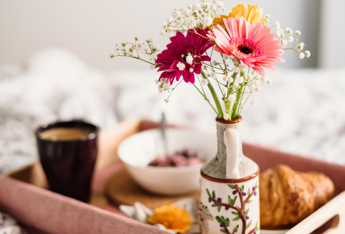 Auf einem Tablett steht eine Vase mit einem bunten Blumenstrauß neben dem Frühstück im Bett.